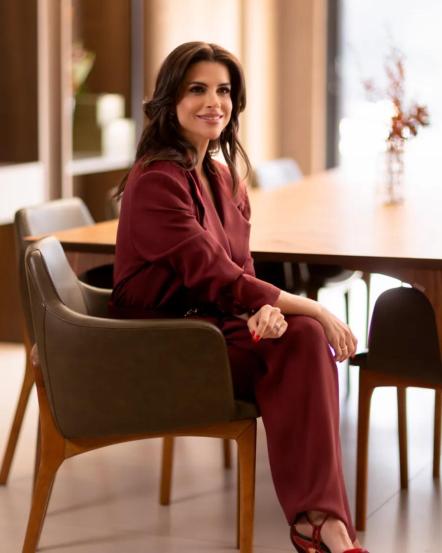 Mel Galhardo sentada à mesa de uma loja, de terno bordô, conversando com clientes durante um Styling Day
