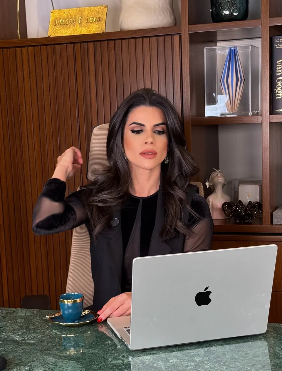 Mel Galhardo trabalhando no notebook, em uma mesa de mármore verde