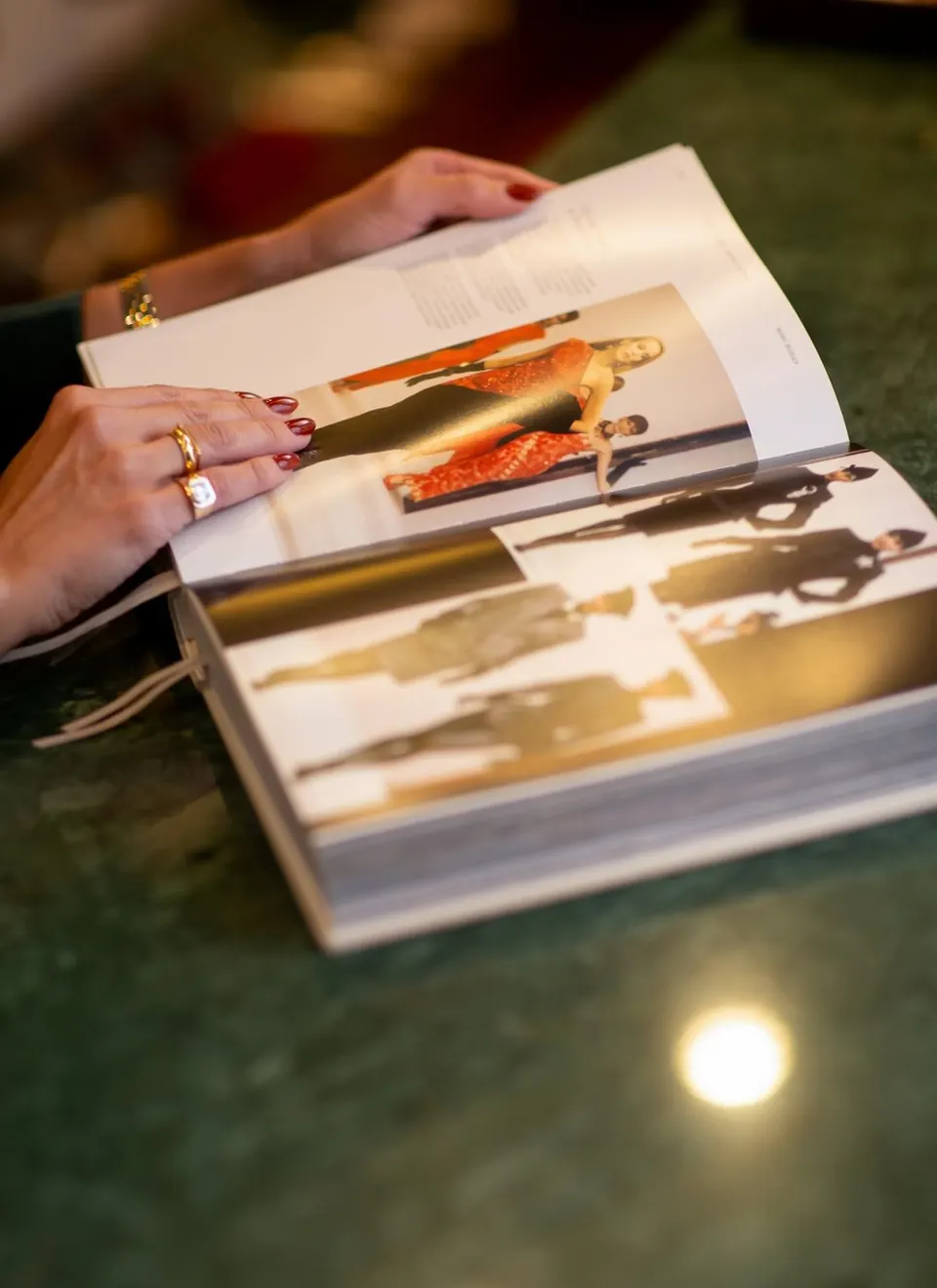 Mãos folheando um lookbook com fotos de moda sobre uma mesa de mármore verde